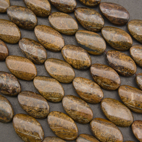 A close-up of polished oval stone beads in earthy brown, tan, and gold tones arranged diagonally on a dark gray background.