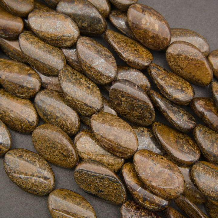 A close-up of polished brown and gold oval stones or beads arranged on a dark gray surface.