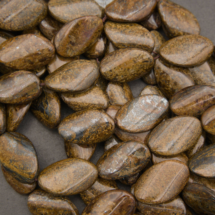 A pile of polished brown and gold jasper stone beads with natural striations, shown in a close-up view on a dark gray background.