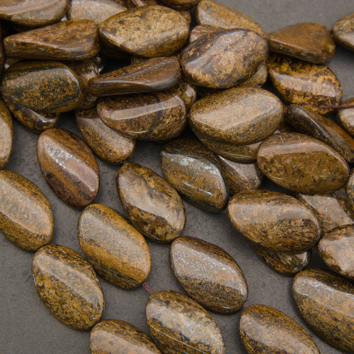 A pile of polished brown and gold pebble-shaped beads or charms with a glossy finish, arranged on a dark gray background.