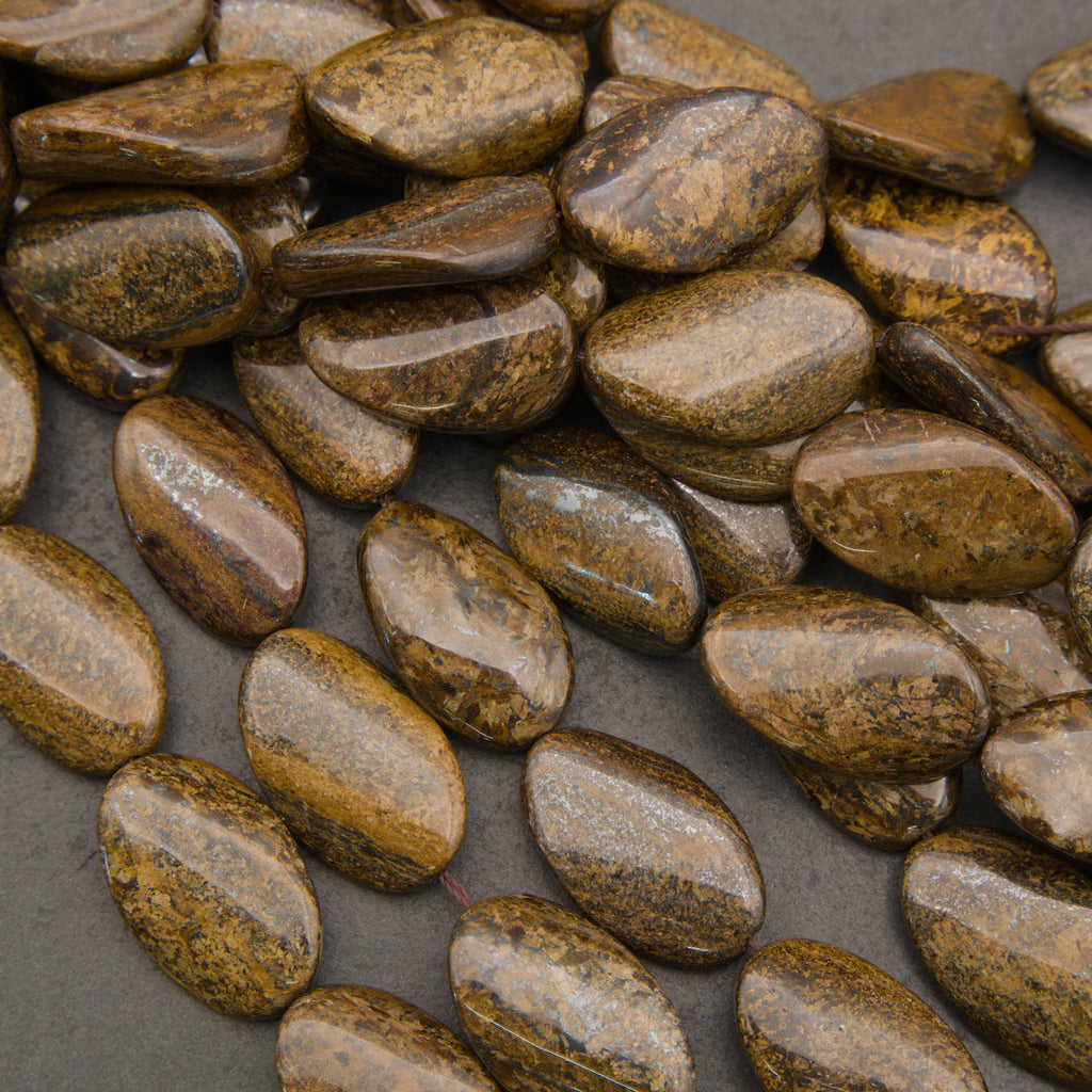 A pile of polished brown and gold pebble-shaped beads or charms with a glossy finish, arranged on a dark gray background.