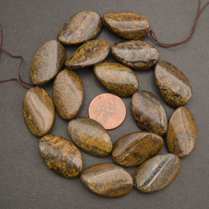 A strand of polished brown and gold jasper stone beads on a dark gray background, with a copper penny in the center for scale.