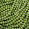 A close-up pile of small, round, light green beads with a glossy finish and minor dark specks.