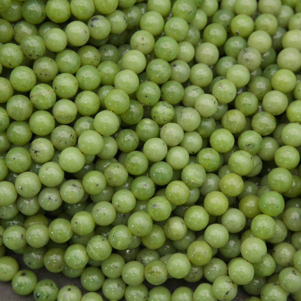 A close-up pile of small, round, light green beads with a glossy finish and minor dark specks.