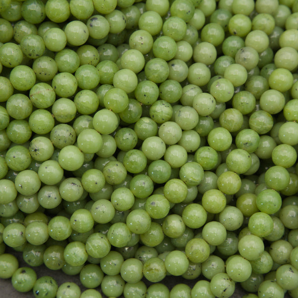 A close-up pile of small, round, light green beads with a glossy finish and minor dark specks.