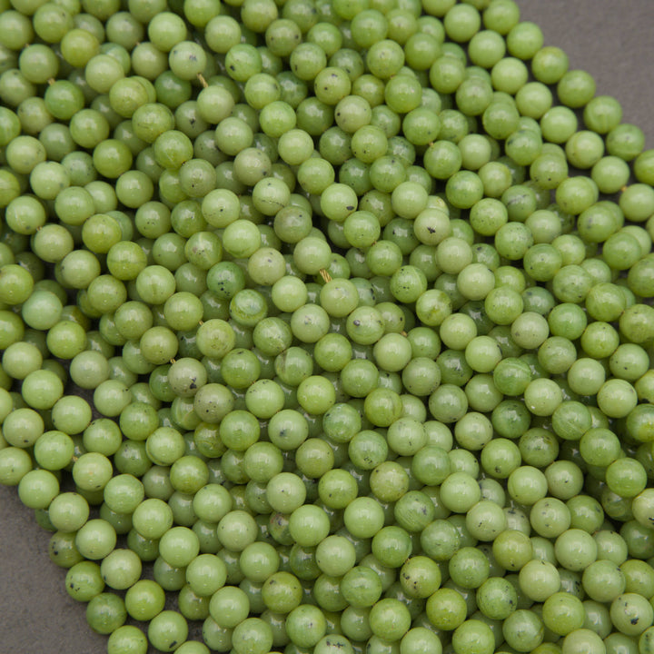 A close-up pile of small, round, light green beads with a glossy finish, filling almost the entire frame against a neutral gray background.