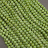 A close-up pile of small, round, light green beads with a glossy finish, filling almost the entire frame against a neutral gray background.