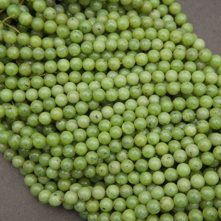 A close-up pile of light green, round, bead-like grapes or grape-like decorative beads on a neutral gray surface.