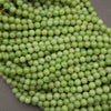 A close-up pile of light green, round, bead-like grapes or grape-like decorative beads on a neutral gray surface.