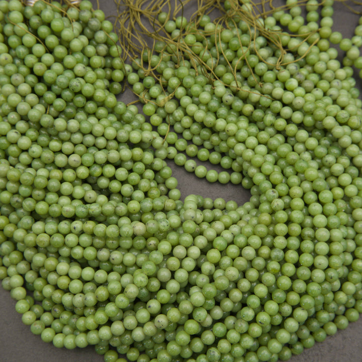 Green round seed beads strung on cords, arranged in loose coils on a neutral gray surface.