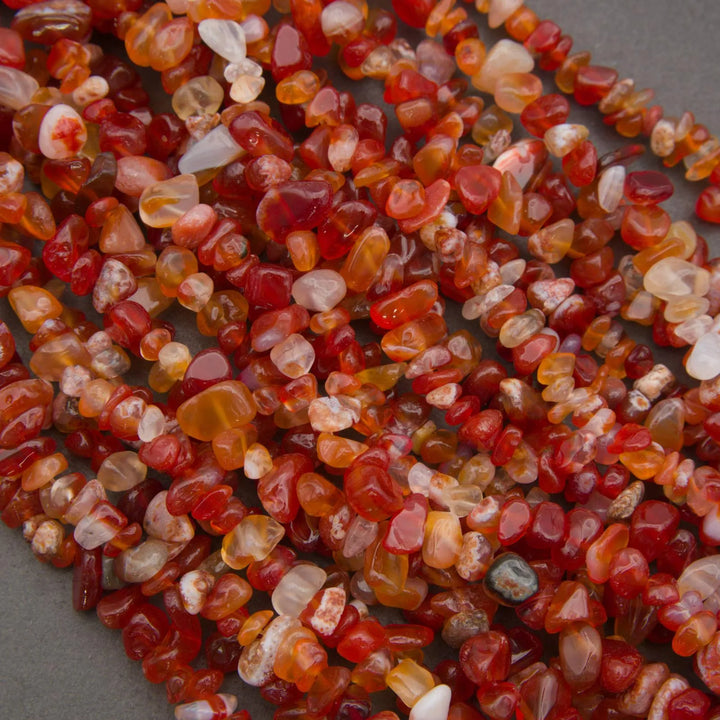 Close-up of a string of red and orange gemstone beads on a gray surface