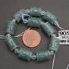 Green jade beads with crystal accents on a string, next to a penny for scale, on a gray background.