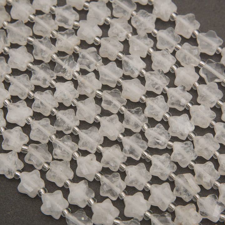 Rows of faceted clear quartz star beads on a gray background, frosty white to water clear