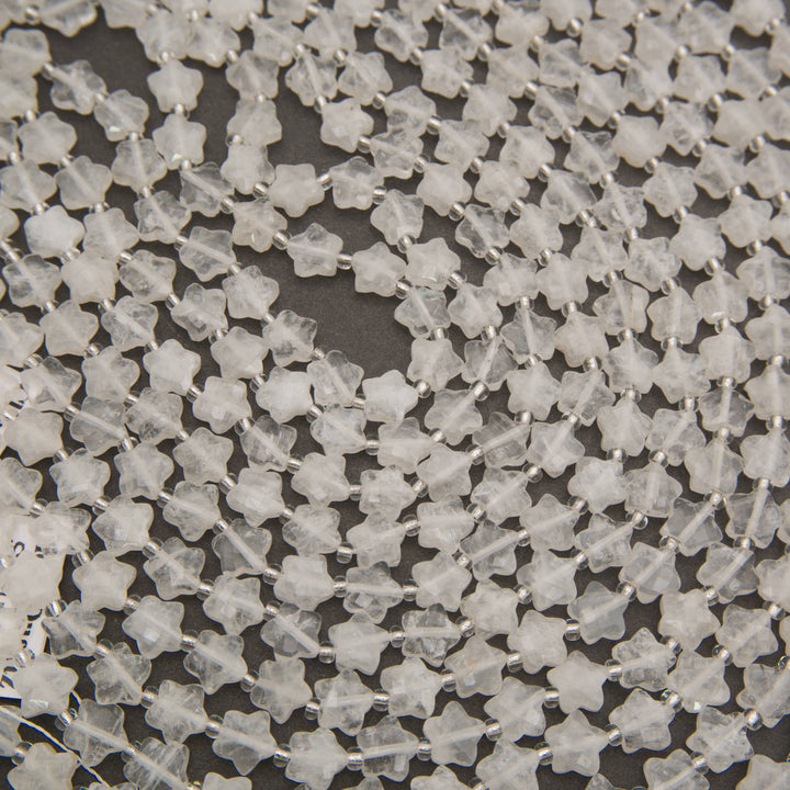 Strands of faceted clear quartz star beads laid in curving rows on a gray background