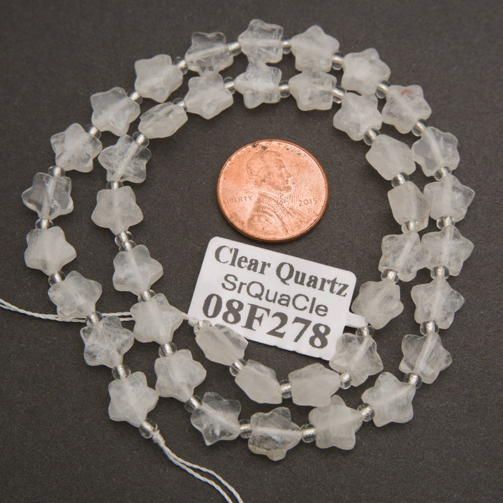 A strand of faceted clear quartz star beads coiled around a penny for scale