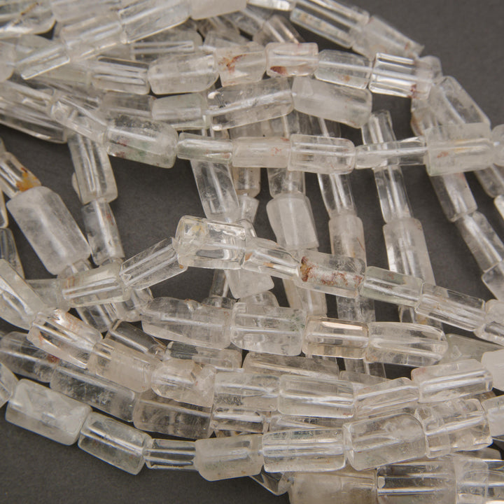 Multiple strands of clear quartz tube beads displaying transparent to milky white coloring and subtle mineral inclusions.