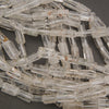 Multiple strands of clear quartz tube beads displaying transparent to milky white coloring and subtle mineral inclusions.