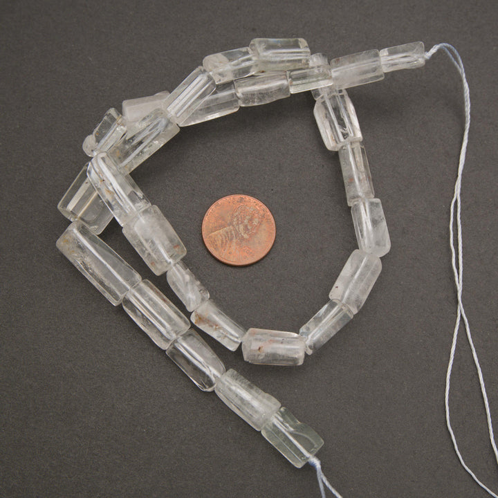 Transparent clear quartz gemstone beads featuring natural fractures, cloudy inclusions, and occasional earthy mineral markings.