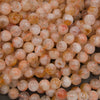 A close-up pile of round, translucent gemstone beads in soft peach, pink, and warm orange tones with natural inclusions.