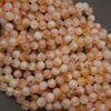 A pile of round, translucent gemstone beads in peach, orange, and cream colors with natural inclusions, photographed close-up on a dark gray background.