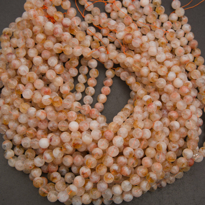Coiled strands of round, polished beads in a peachy-pink, white, and light orange marbled pattern, strung together on orange cord against a dark gray background.