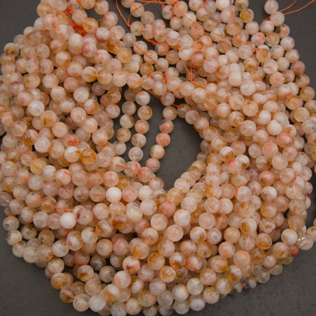 Coiled strands of round, polished beads in a peachy-pink, white, and light orange marbled pattern, strung together on orange cord against a dark gray background.