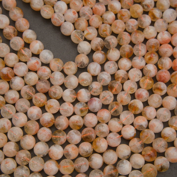 Round faceted gemstone beads in a peachy-orange and cream color mix with natural inclusions, arranged on a dark gray background.