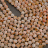 Round faceted gemstone beads in a peachy-orange and cream color mix with natural inclusions, arranged on a dark gray background.