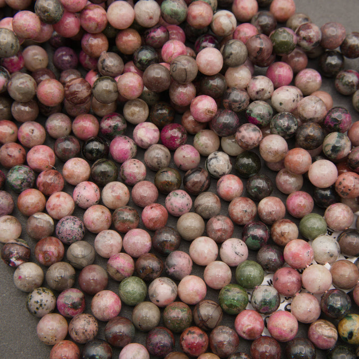 Rows of smooth round cobalto calcite beads on a gray background in pink, brown and olive green