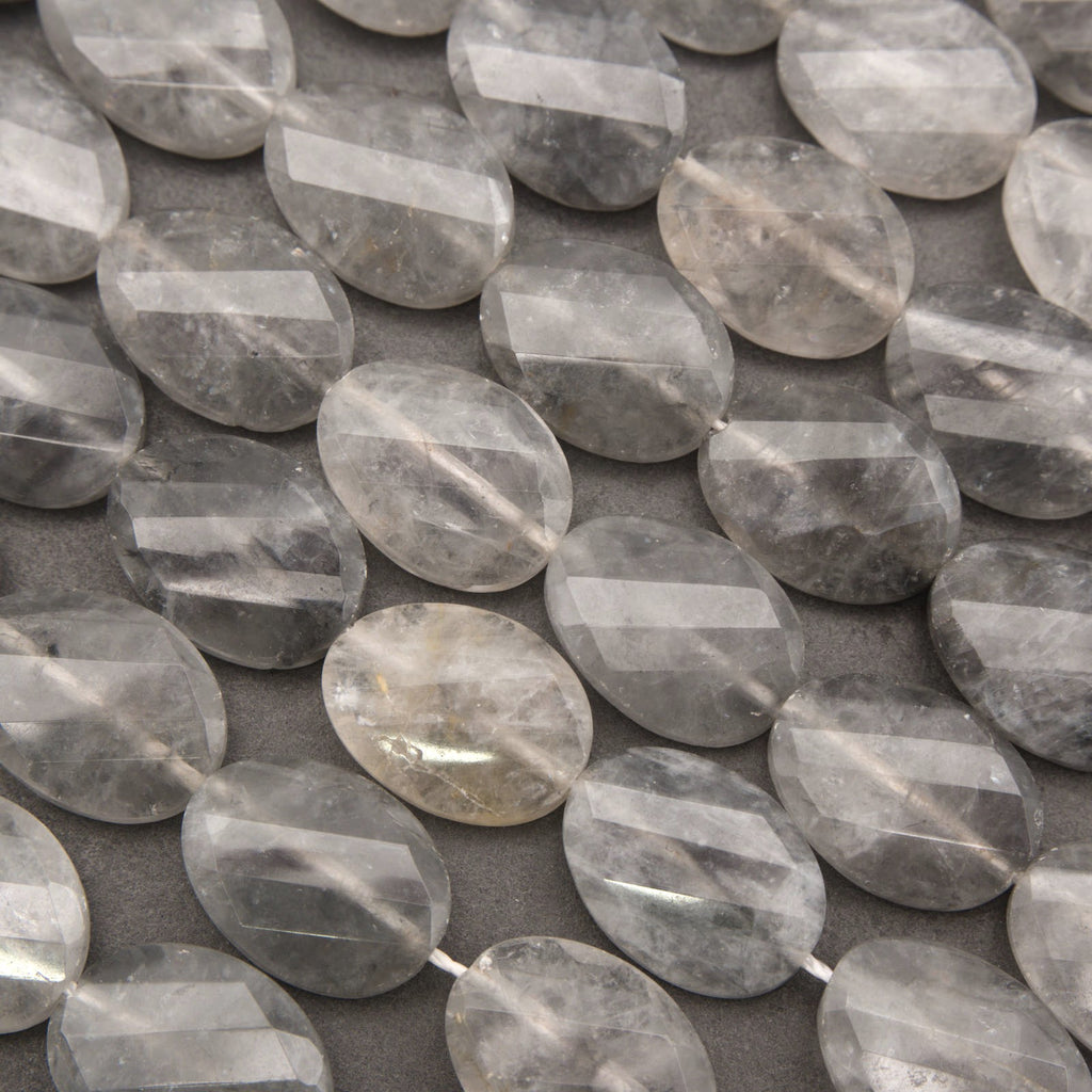 Faceted oval clear quartz gemstone beads arranged in rows on a dark gray background.