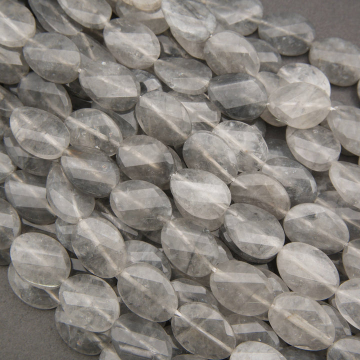 Faceted round clear quartz beads with natural inclusions, piled together on a dark gray background.