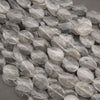 Faceted round clear quartz beads with natural inclusions, piled together on a dark gray background.