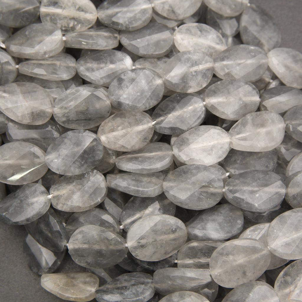 A pile of faceted oval gemstone beads in a translucent smoky gray color, showing natural inclusions and a polished finish.