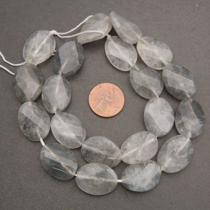 Faceted gray smoky quartz gemstone beads on a white cord, shown with a US penny for scale on a dark gray background.