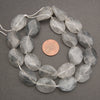 Faceted gray smoky quartz gemstone beads on a white cord, shown with a US penny for scale on a dark gray background.