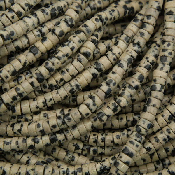 Polished dalmatian jasper heishi beads with cream and black speckled pattern on a neutral background.