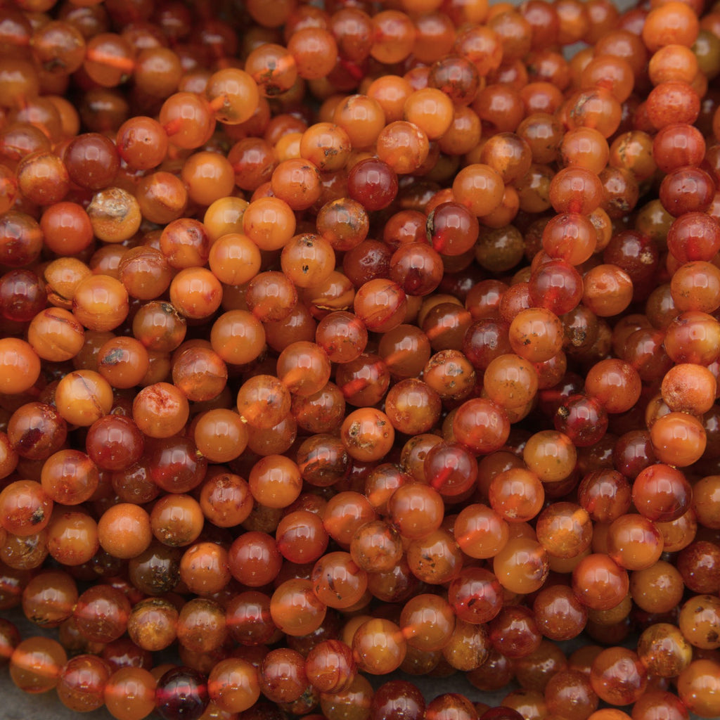 A close-up pile of small round beads in warm amber, orange, and reddish-brown tones with glossy highlights.