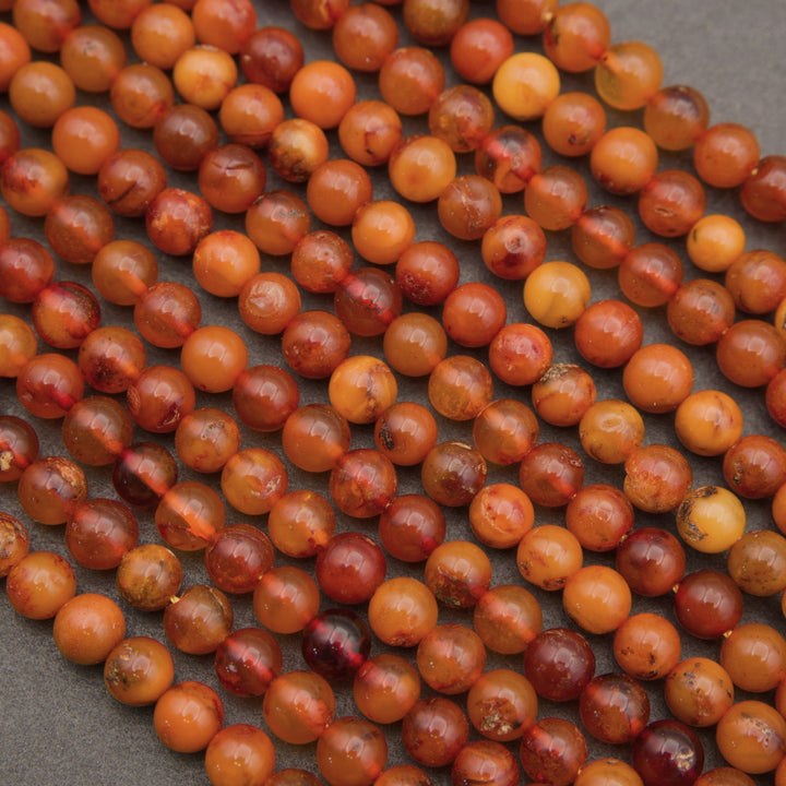 Close-up of multiple strands of round amber beads in warm orange, brown, and reddish tones on a dark gray background.