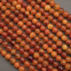 Close-up of multiple strands of round amber beads in warm orange, brown, and reddish tones on a dark gray background.