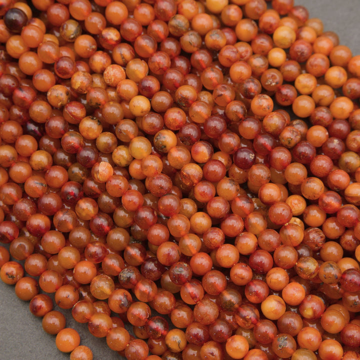 A close-up pile of small, round, polished beads in warm orange, amber, and reddish-brown tones with some marbled variation.