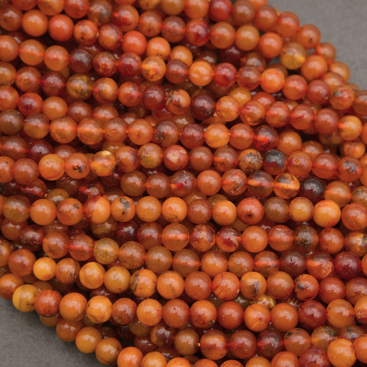 A close-up pile of round, polished beads in warm amber, orange, and reddish-brown tones with natural marbling and inclusions.