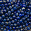 A close-up pile of polished round beads made of lapis lazuli, showing deep blue and white marbled patterns with tiny golden flecks.
