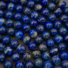 A close-up pile of polished spherical beads in lapis lazuli, showing deep blue with white marbling and subtle golden flecks, resting on a dark surface.