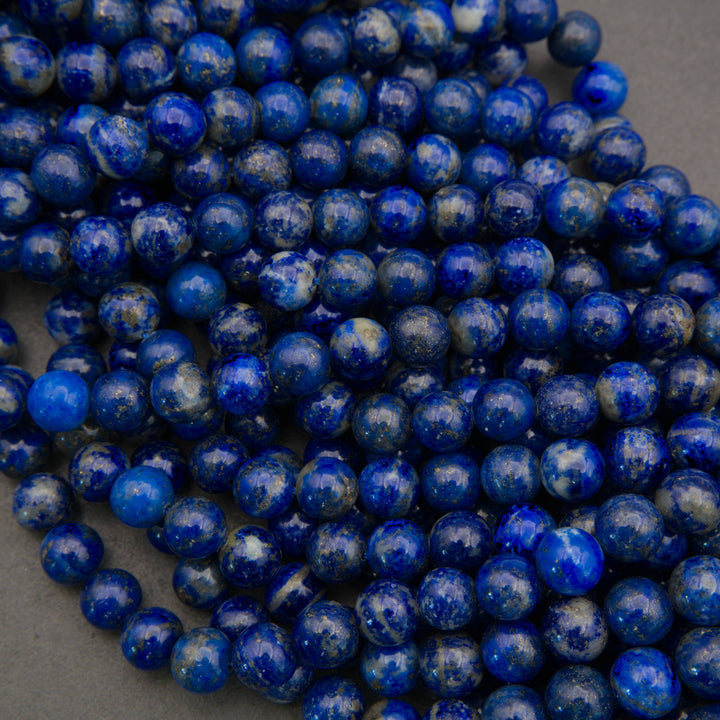 A pile of round, polished lapis lazuli crystal beads with natural white and gray veining on a dark gray background.