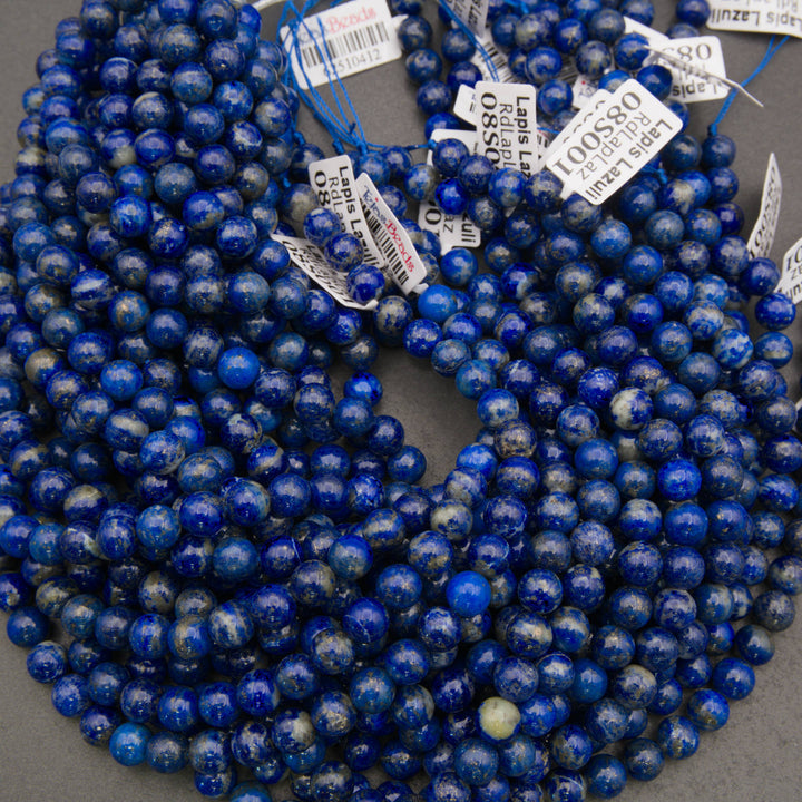 Multiple strands of round lapis lazuli crystal beads in deep blue with white flecks, coiled together on a gray surface with product tags attached.