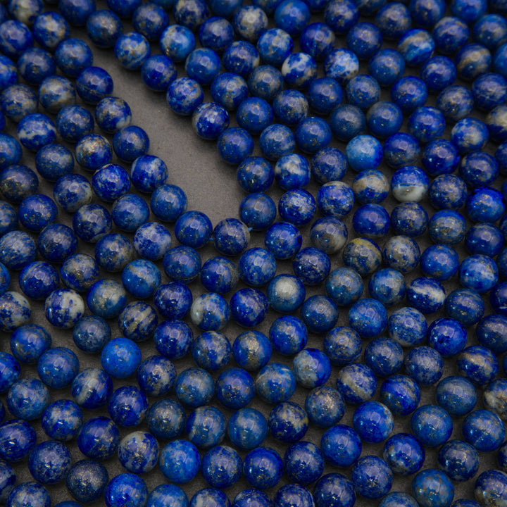 Close-up of many small round blue beads with white speckling, arranged on a dark gray surface.