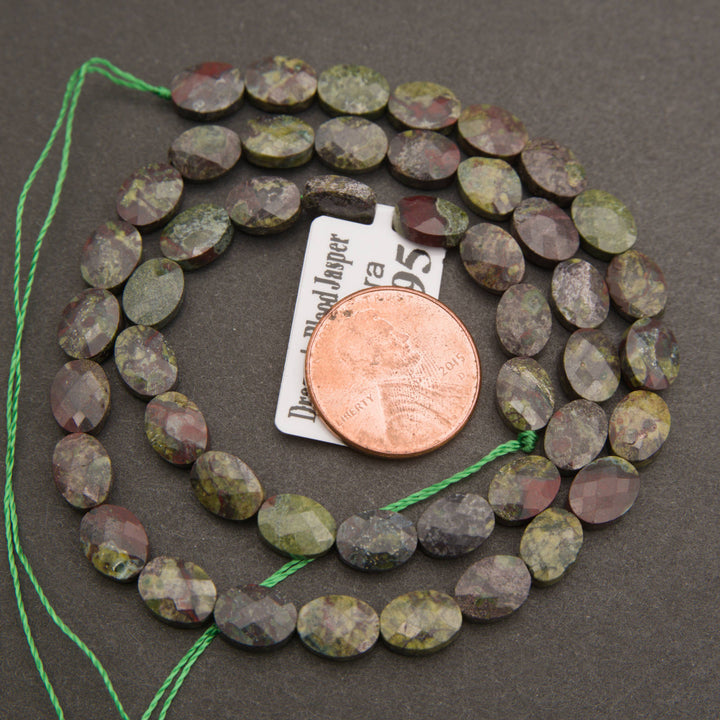 A strand of faceted dragon's blood jasper oval beads coiled around a penny for scale