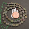 A strand of faceted dragon's blood jasper oval beads coiled around a penny for scale