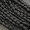 Close-up of black lava rock oval beads featuring elongated shapes and distinctive volcanic pitting.