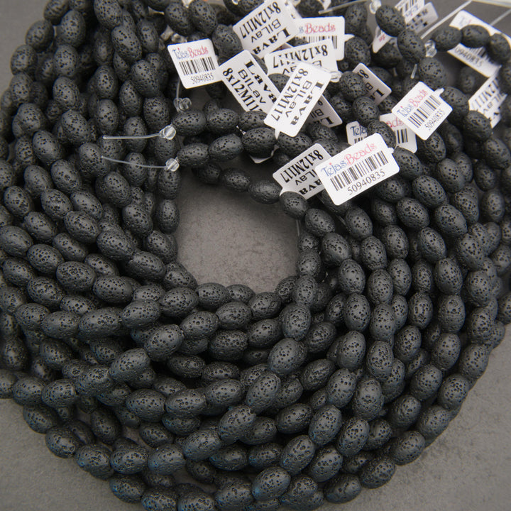 Multiple strands of matte black lava stone oval beads showcasing natural pores and charcoal-black surfaces.